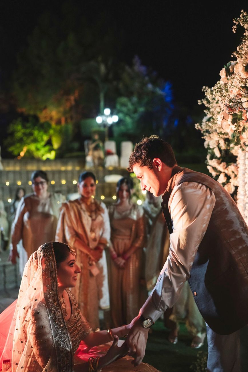 Groom leaning down to take the bride's hand just after the nikah ceremony, family members standing behind, Nayha & Rafay's wedding in Islamabad