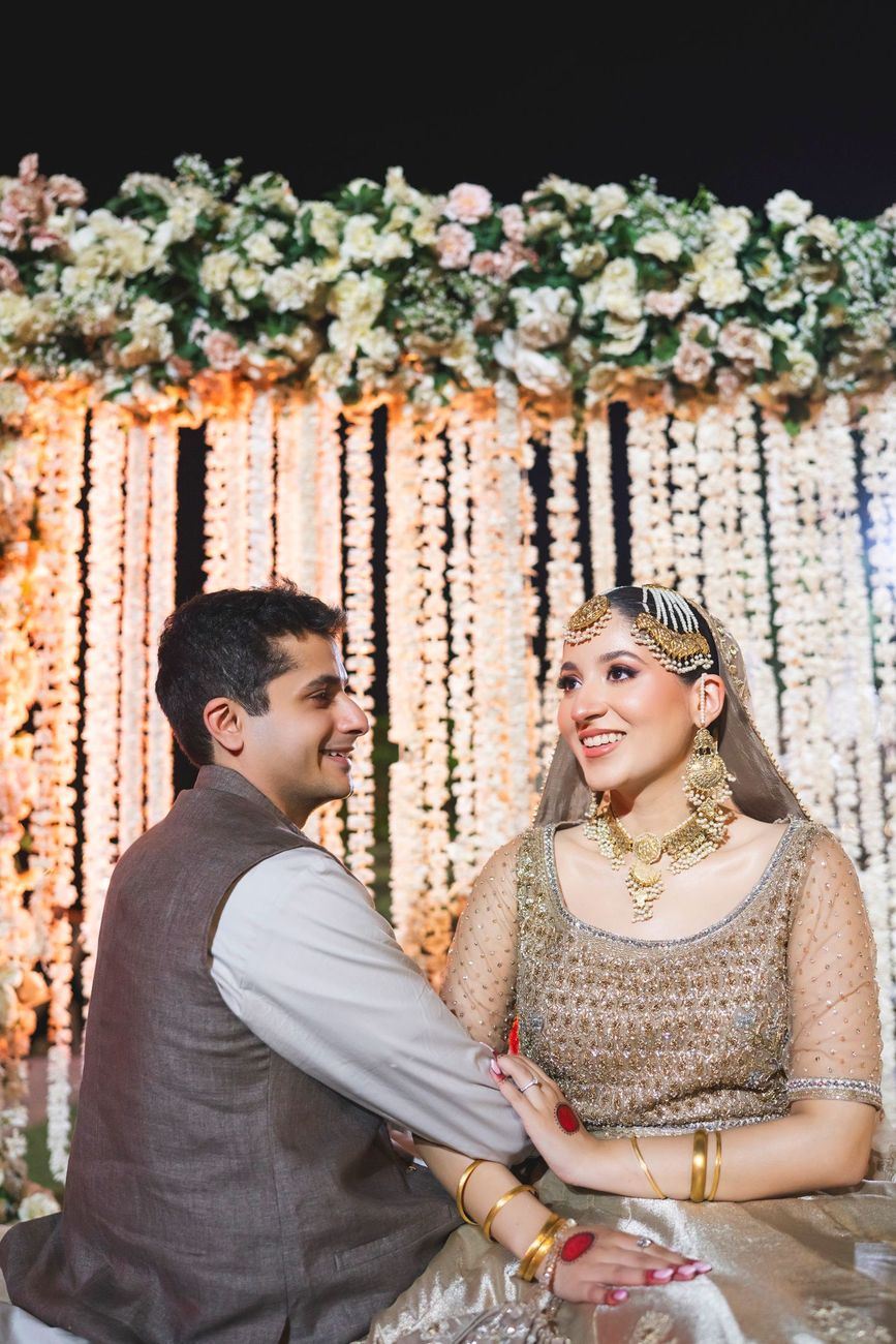 Bride and groom smiling at each other in front of a hanging floral curtain backdrop after the nikah, Nayha & Rafay's wedding in Islamabad