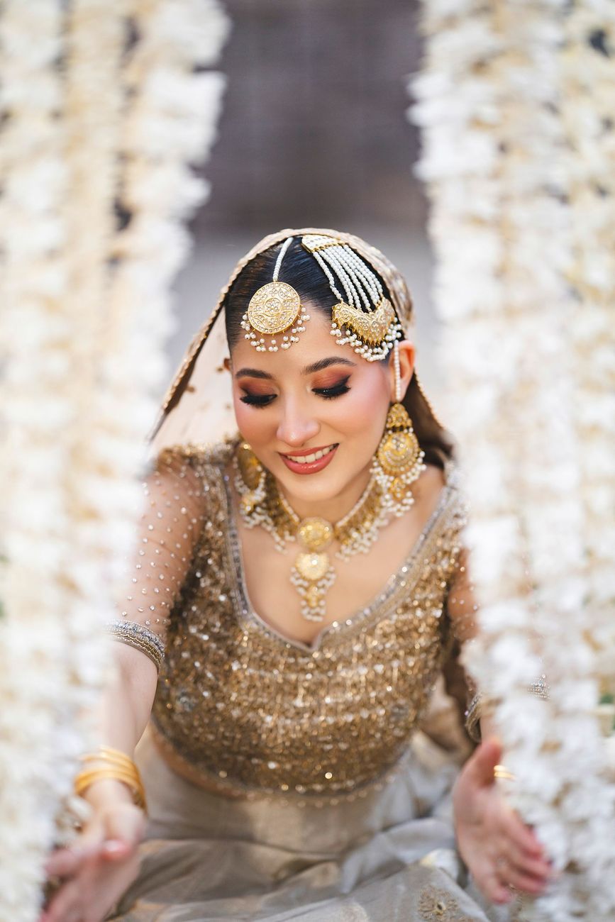 Close-up bridal portrait framed between hanging strands of jasmine garlands, Nayha & Rafay's wedding in Islamabad
