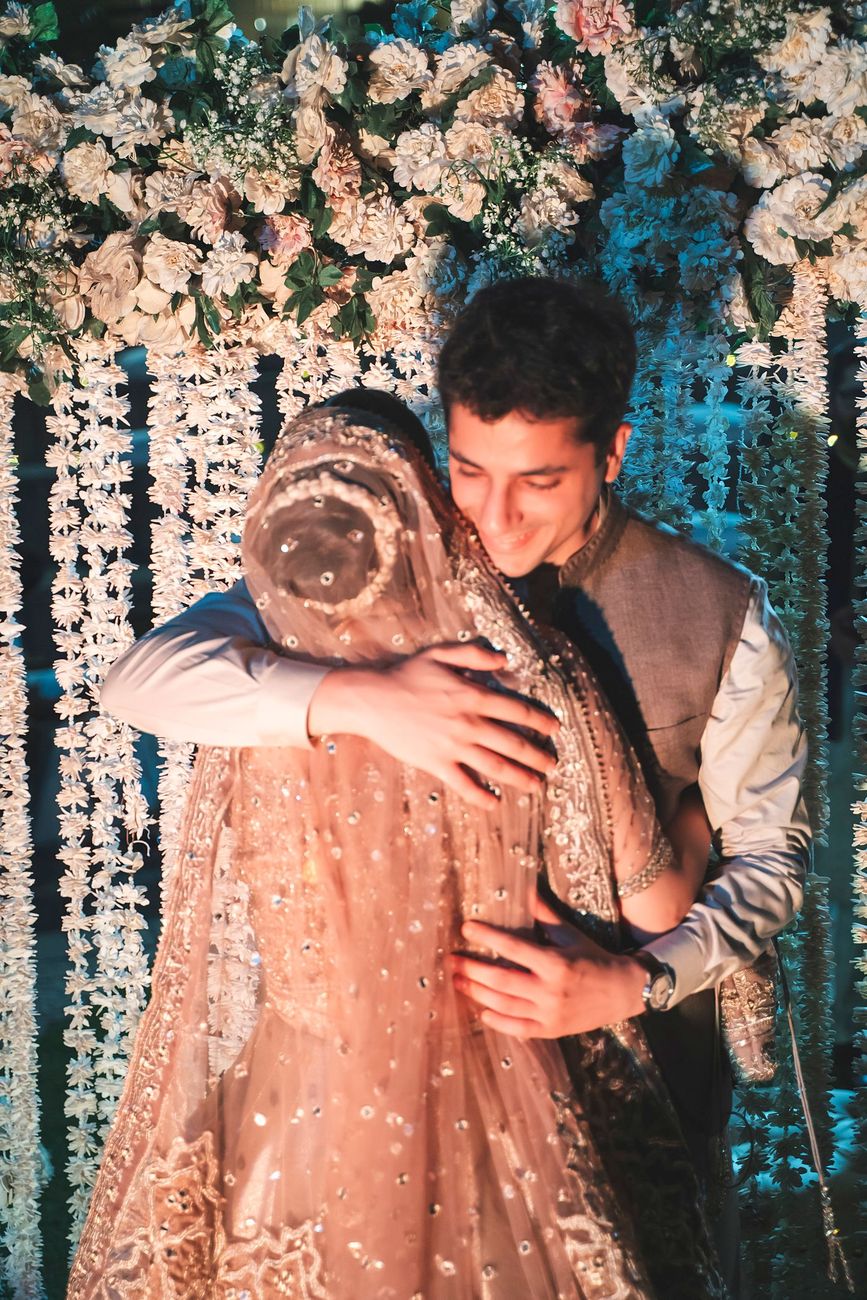 Groom embracing the bride tenderly in front of the floral garland backdrop, Nayha & Rafay's wedding in Islamabad