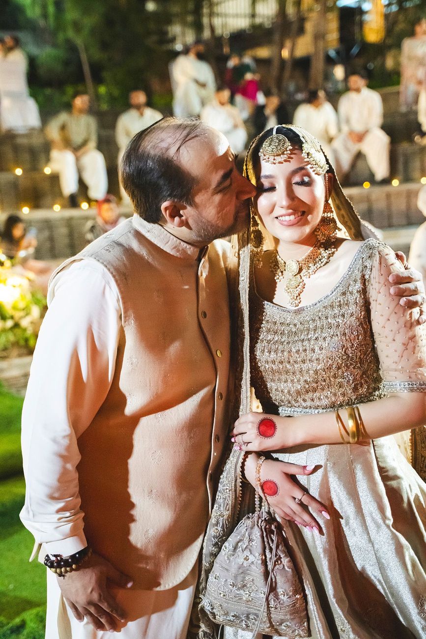 Bride's father kissing her forehead as guests look on from the amphitheater seating, Nayha & Rafay's wedding in Islamabad