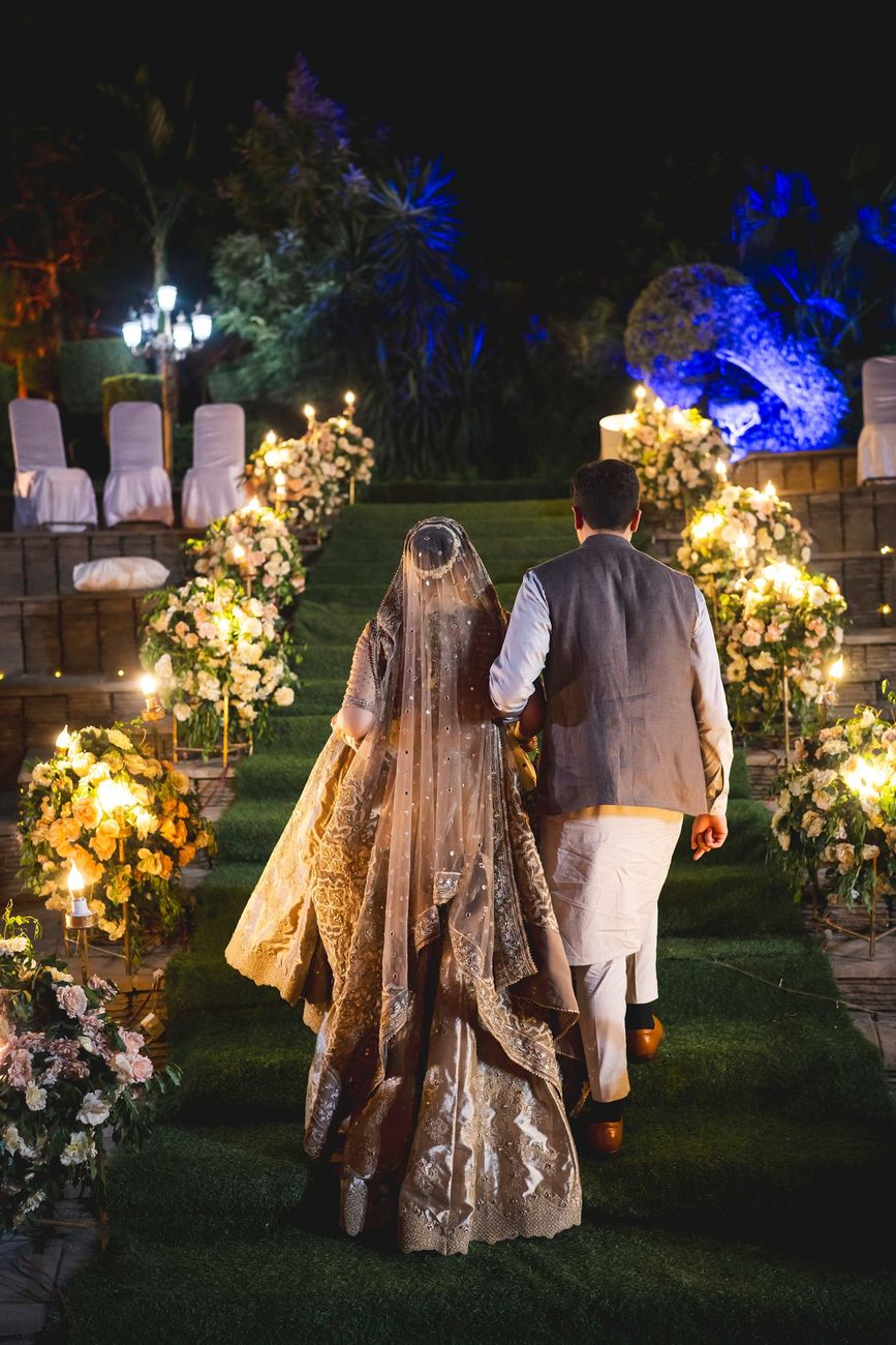 Bride and groom viewed from behind walking up the candle-lit grass staircase at night, Nayha & Rafay's wedding in Islamabad
