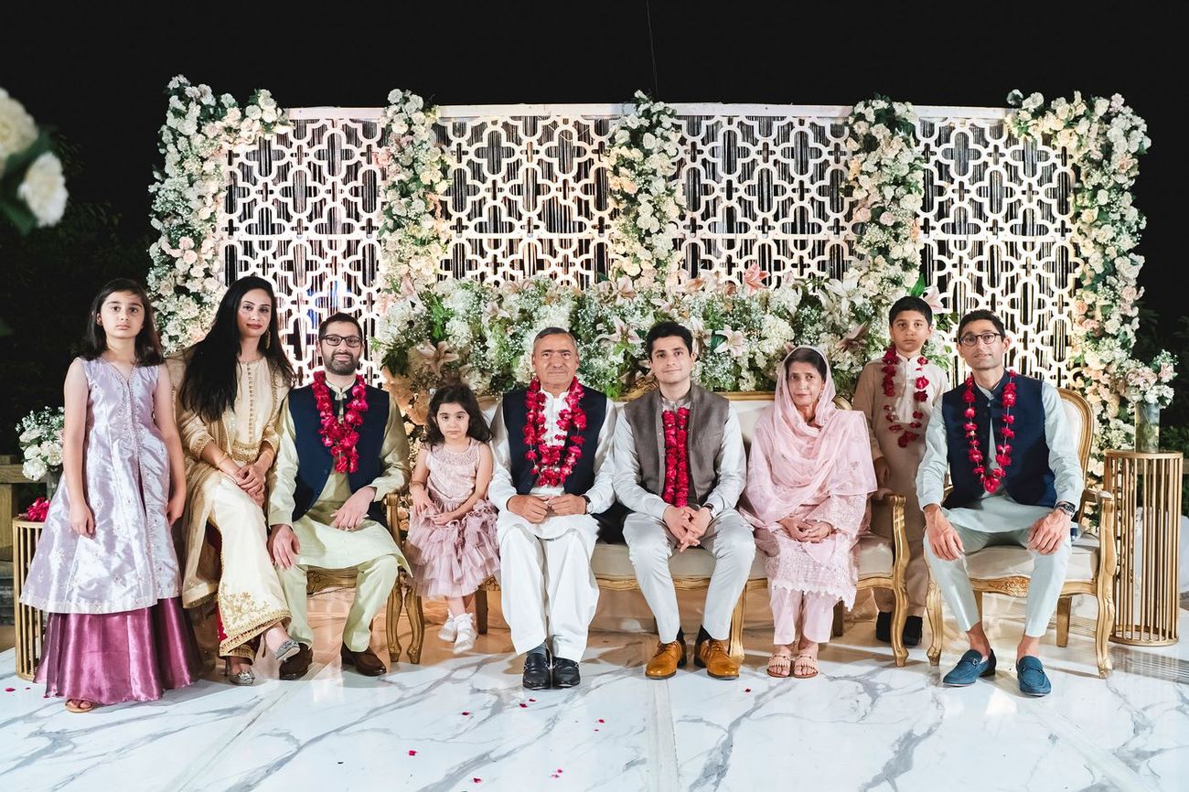 Formal group portrait of the groom's family seated together in front of a floral wall, Nayha & Rafay's wedding in Islamabad