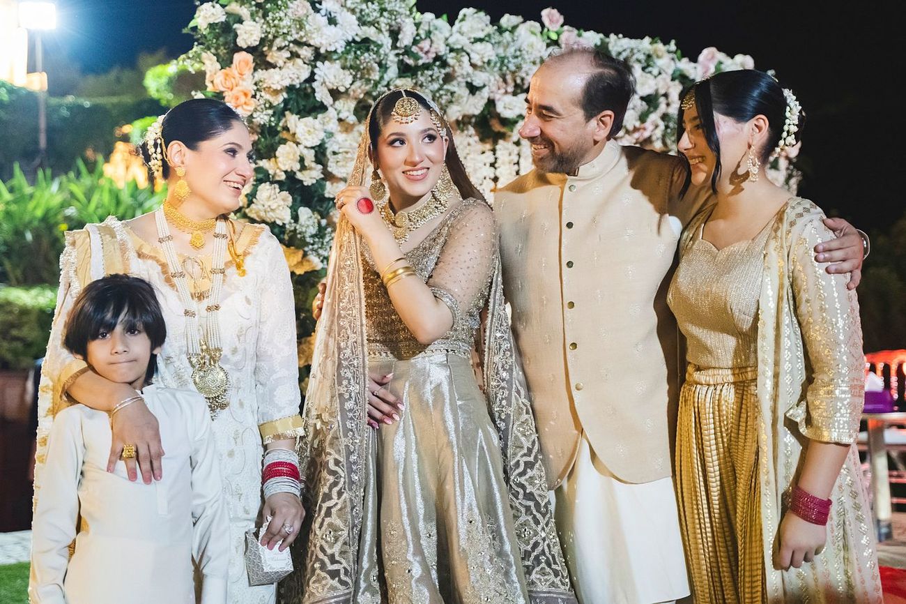 Bride posing with her family members in front of a floral backdrop, smiling together, Nayha & Rafay's wedding in Islamabad