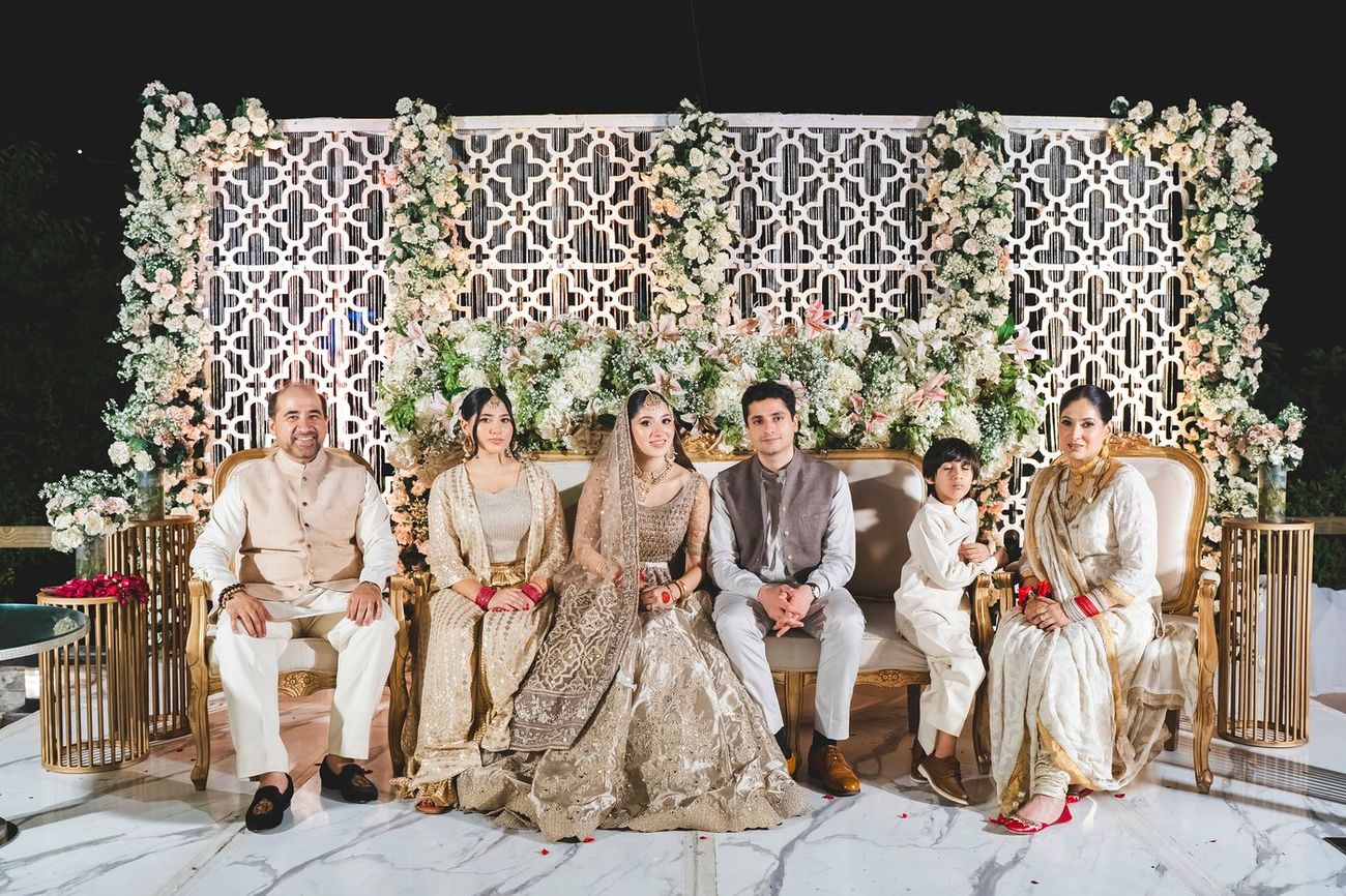Formal group portrait of the bride with her family seated together in front of a floral wall, Nayha & Rafay's wedding in Islamabad