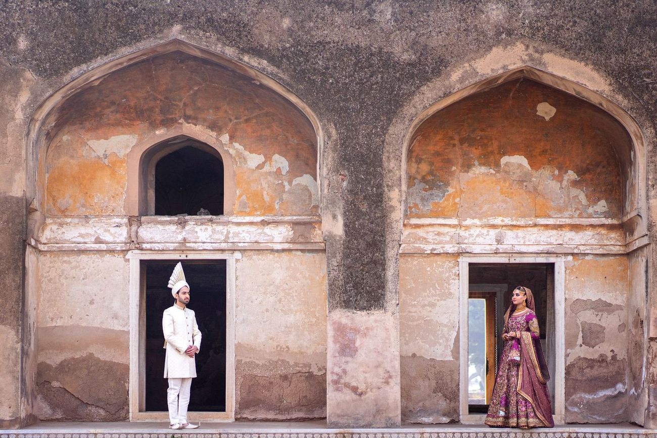 Bride and groom standing in two separate weathered archway doorways at Lahore Fort, facing each other across the gap, Samar & Anoosh's wedding at Lahore Fort