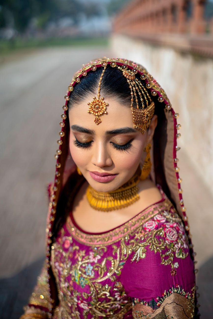 Close-up bridal portrait wearing a gold matha patti and choker, eyes closed, walking along the fort's brick colonnade, Samar & Anoosh's wedding at Lahore Fort