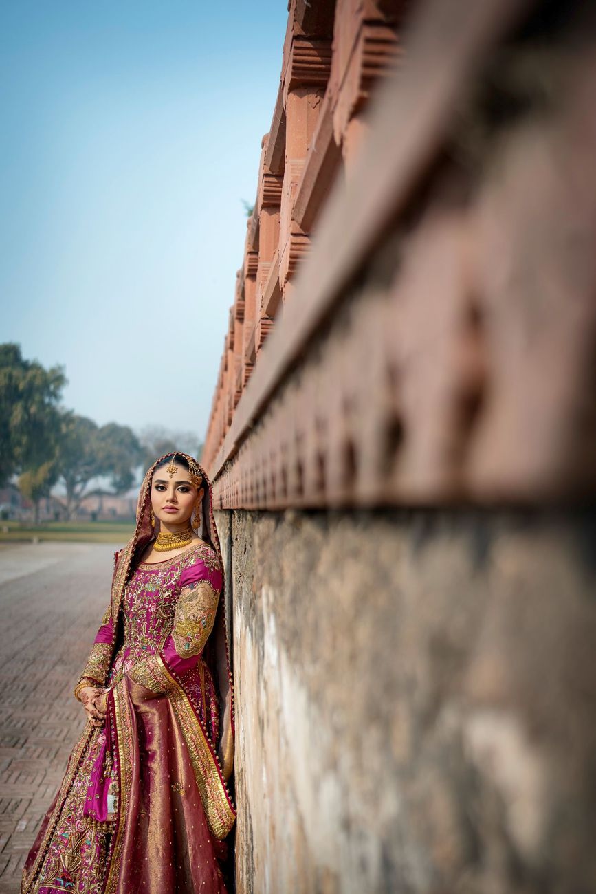 Solo bridal portrait leaning against a red sandstone wall, Samar & Anoosh's wedding at Lahore Fort