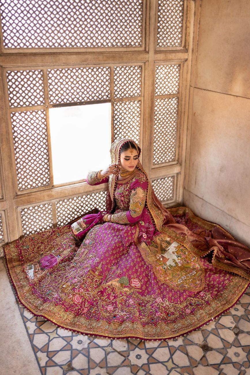 Bride seated beside a carved jali window, her embroidered magenta lehenga spread across the geometric marble floor, Samar & Anoosh's wedding at Lahore Fort