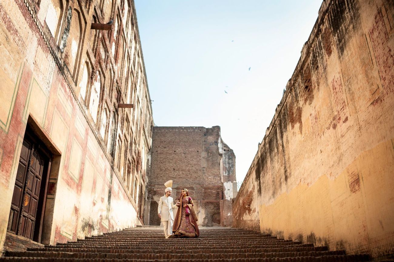 Wide shot of bride and groom walking down a long brick staircase between weathered fort walls, Samar & Anoosh's wedding at Lahore Fort