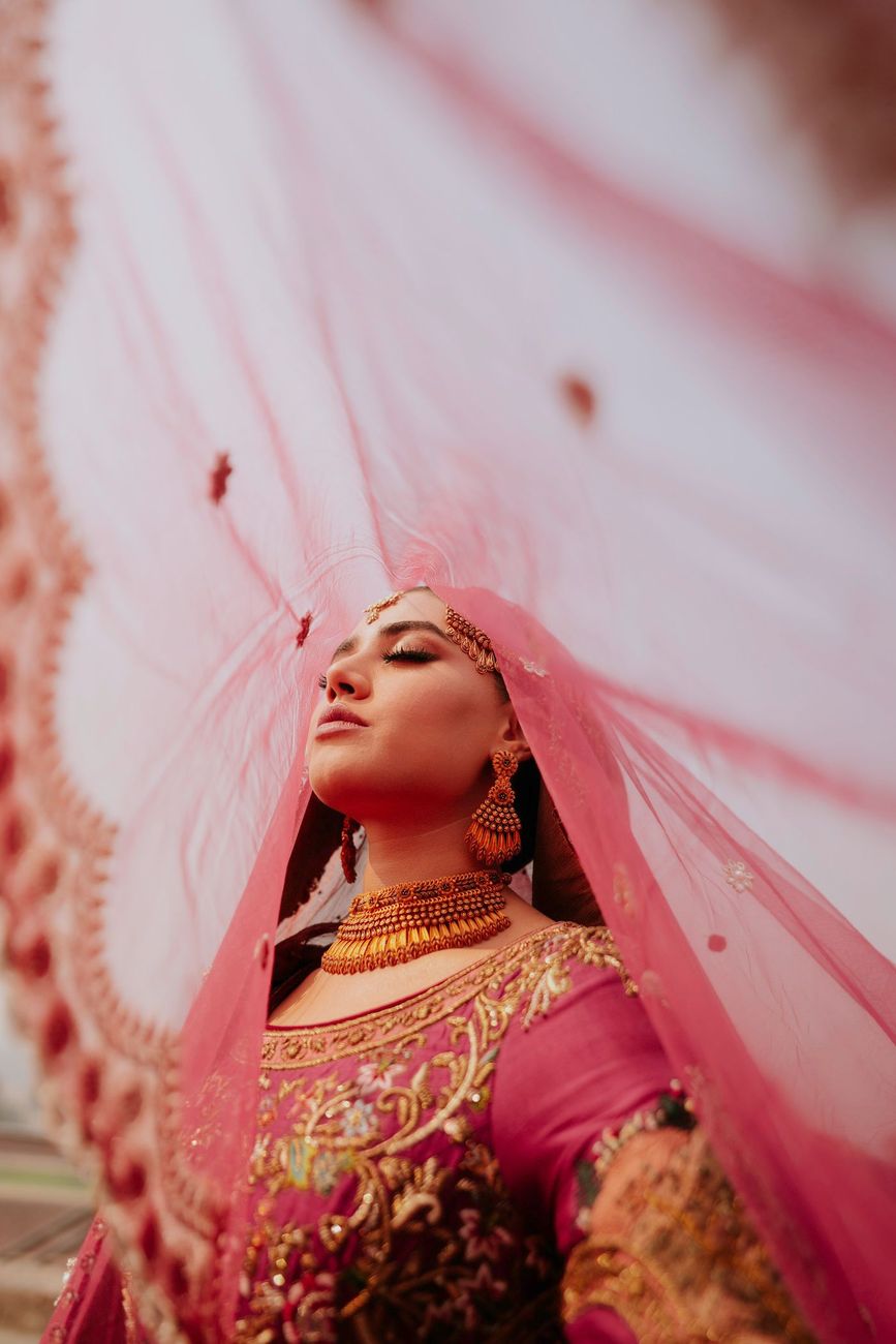 Low-angle close-up of the bride with eyes closed, her maroon dupatta billowing overhead, Samar & Anoosh's wedding at Lahore Fort
