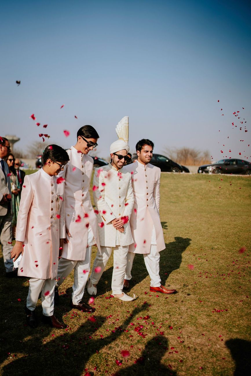 Groom walking across the lawn with his groomsmen as rose petals shower down around them, Samar & Anoosh's wedding