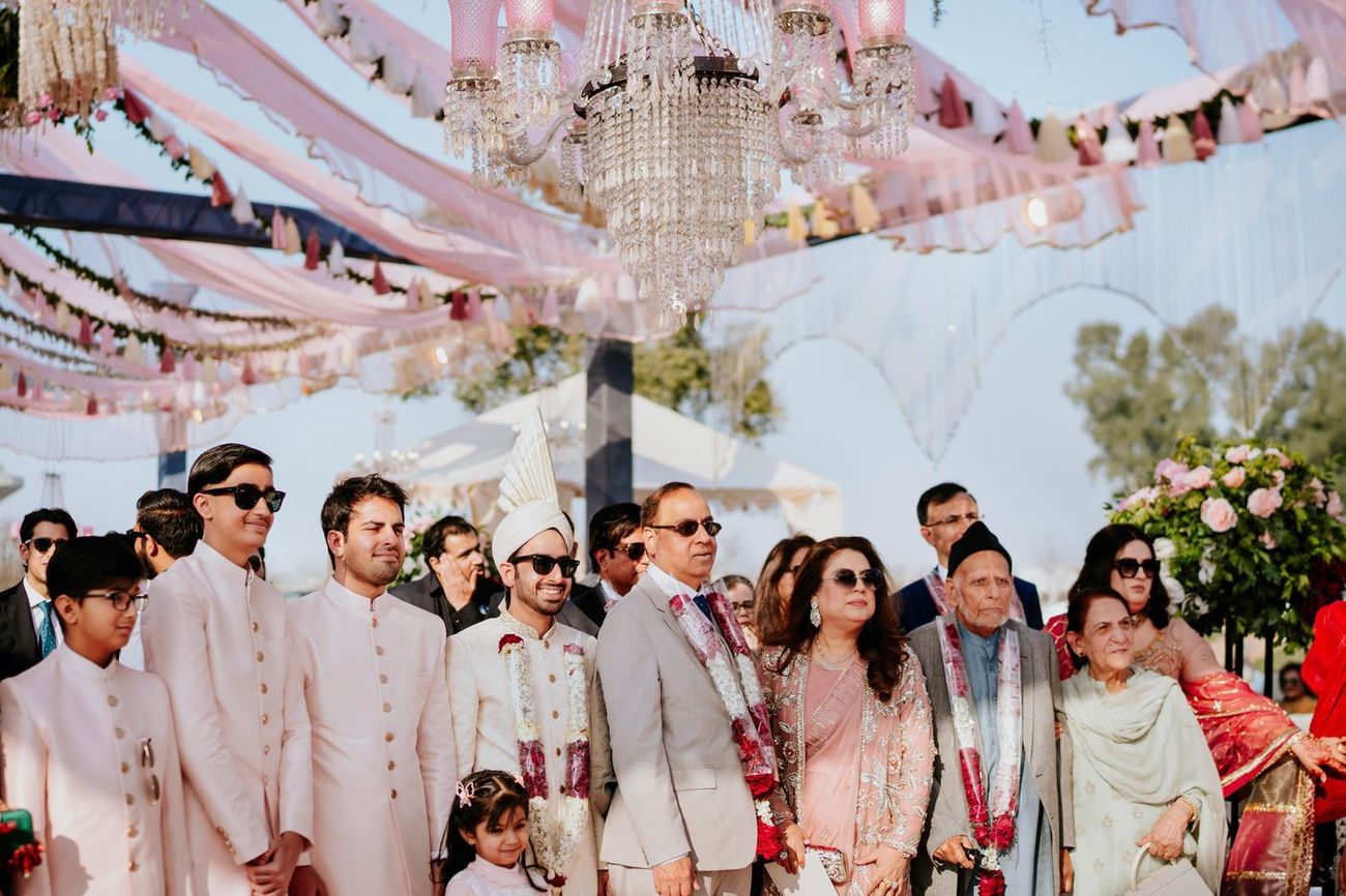 Family group portrait beneath a draped pink fabric canopy and crystal chandeliers at the outdoor wedding venue, Samar & Anoosh's wedding