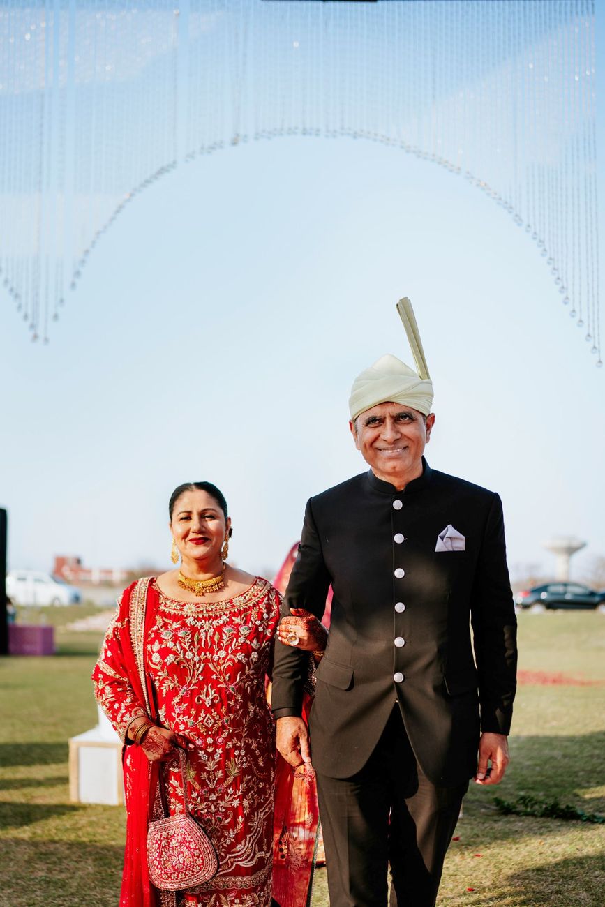 Groom's parents walking arm in arm across the lawn, his mother in a red embroidered outfit, Samar & Anoosh's wedding