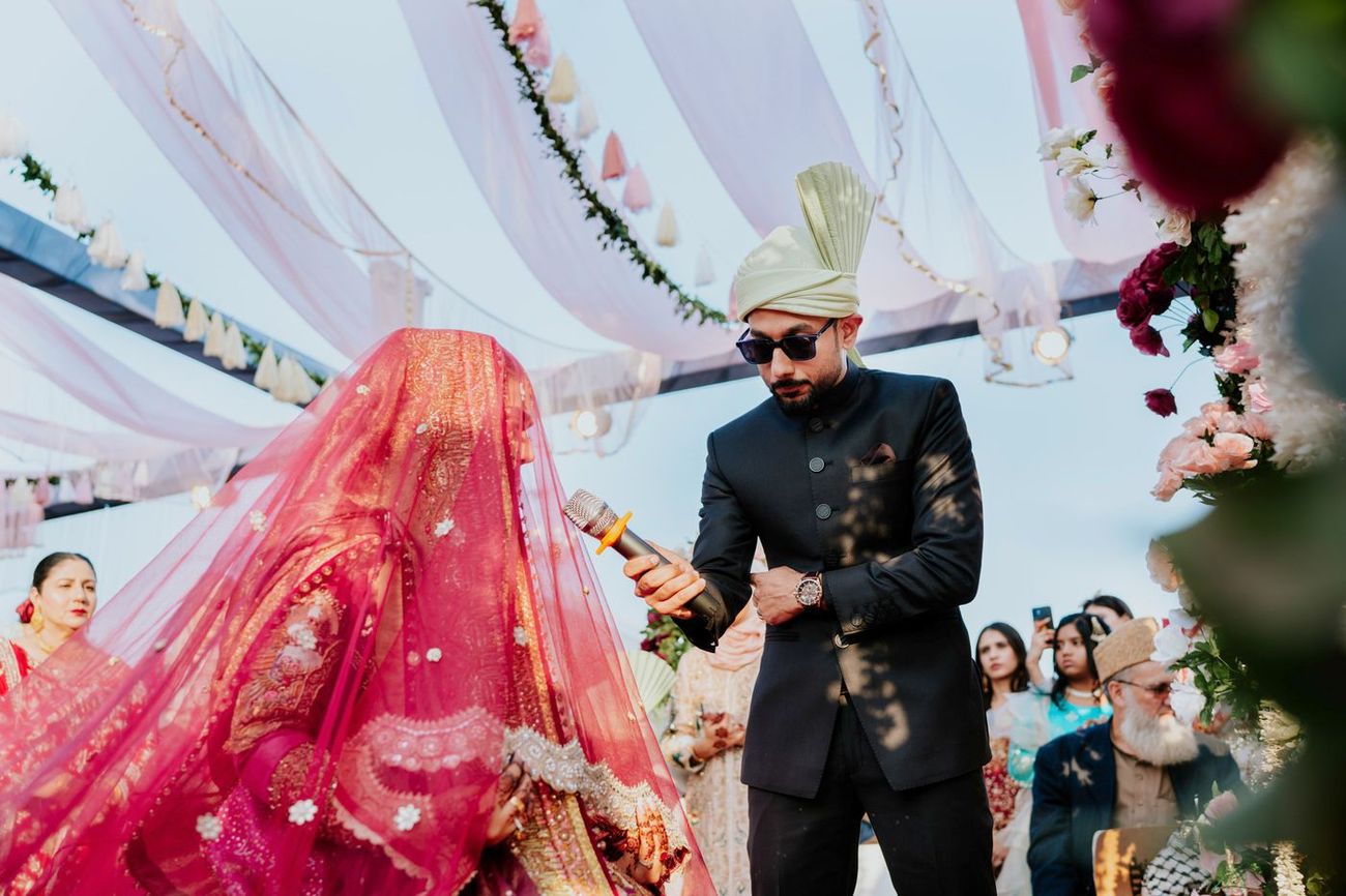 A guest holding a microphone for the veiled, seated bride during her nikah vows