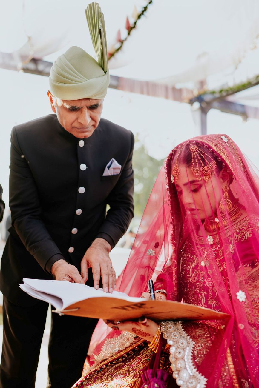 Bride signing the nikah register book as an older male relative points to where to sign