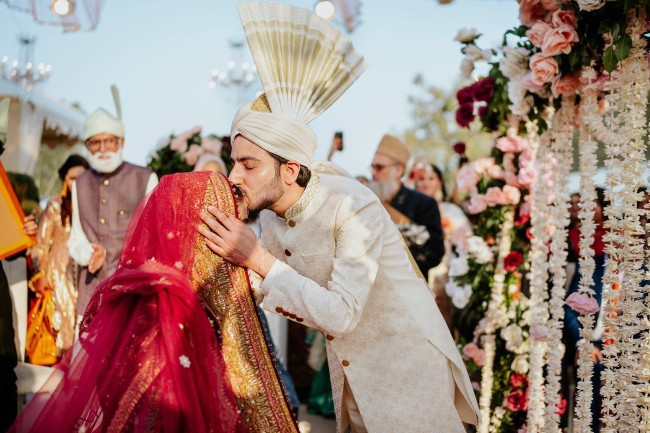 Groom kissing the veiled bride's forehead just after the nikah, guests and floral garlands surrounding them