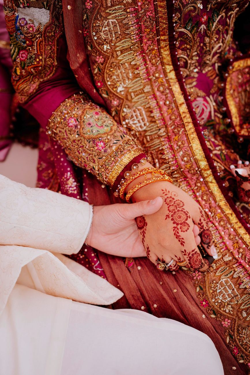 Detail of the groom's hand resting over the bride's henna-painted hand and gold bangles