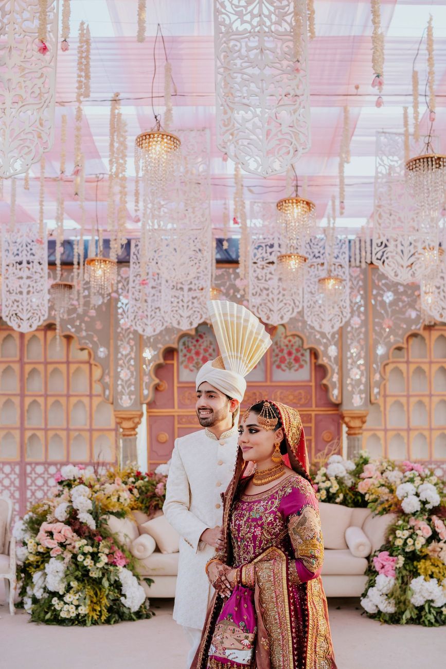 Bride and groom walking together past the reception sofa with its floral arrangements and arched backdrop