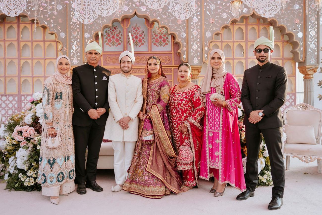Group photo of the bride, groom, and five family members standing in front of the reception stage backdrop