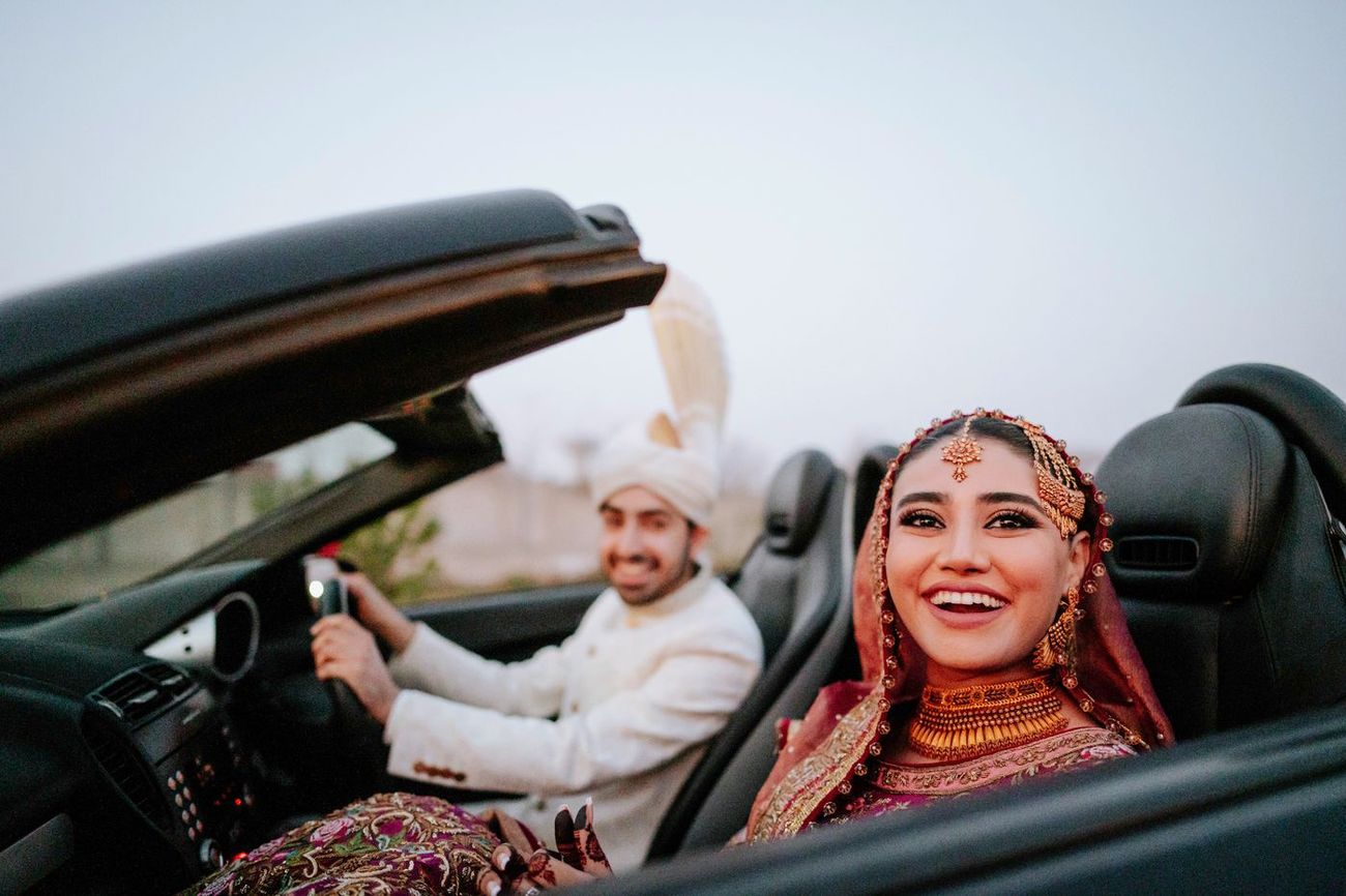 Bride and groom riding off together in an open-top car, both laughing
