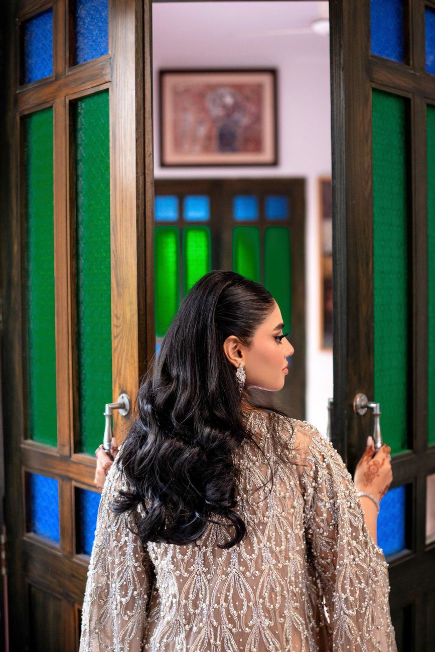 Bride seen from behind opening a pair of stained-glass doors, her hair styled in loose waves