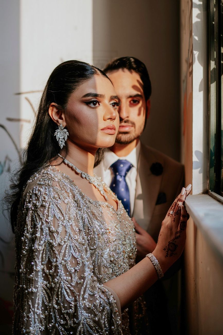 Close-up of the bride and groom standing together by a sunlit window, her hand resting on the windowsill