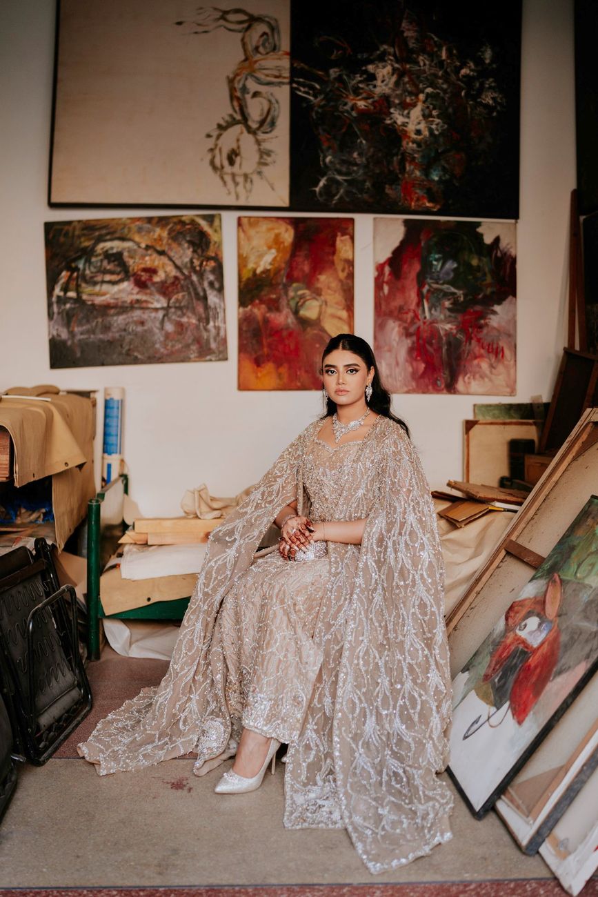 Solo bridal portrait seated amid stacked canvases and paintings in the art studio
