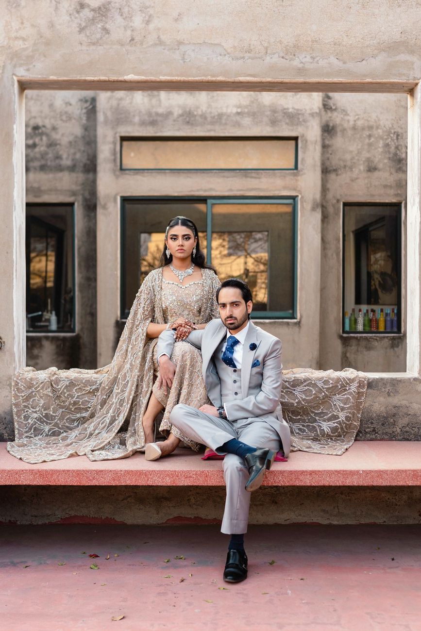 Couple seated together on a pink stone bench in front of a weathered building facade