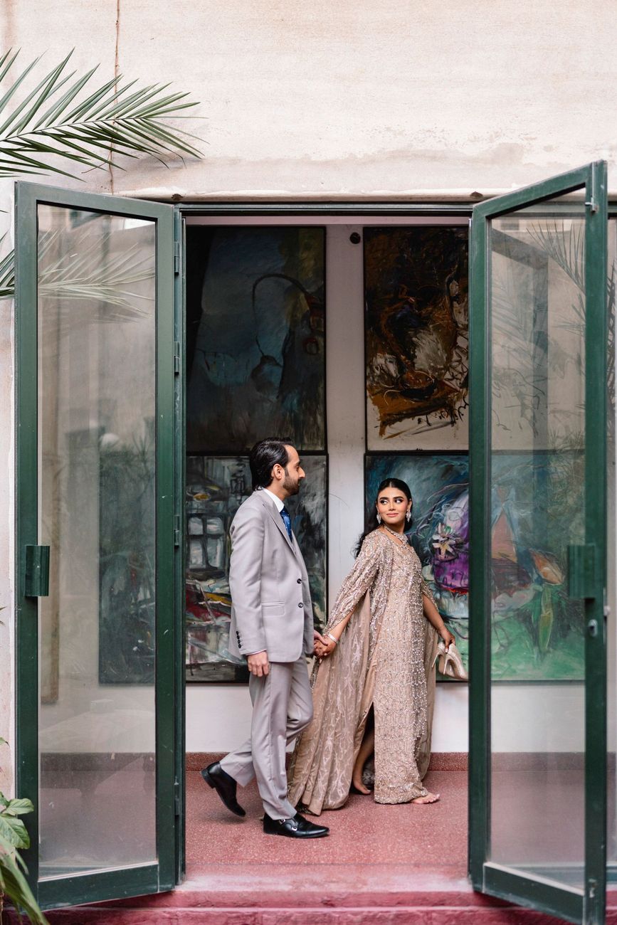 Couple holding hands in a doorway lined with abstract paintings, the bride glancing back over her shoulder