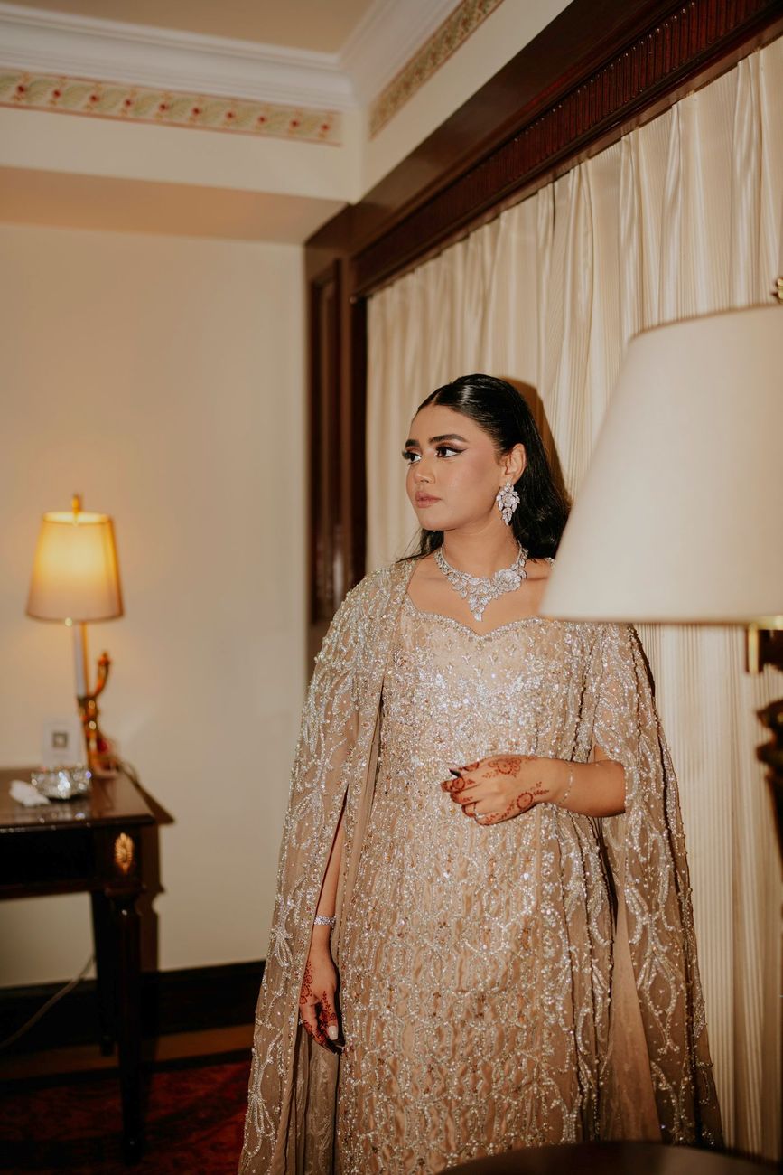 Solo bridal portrait in a hotel suite, looking off to the side beside a lamp and curtained window