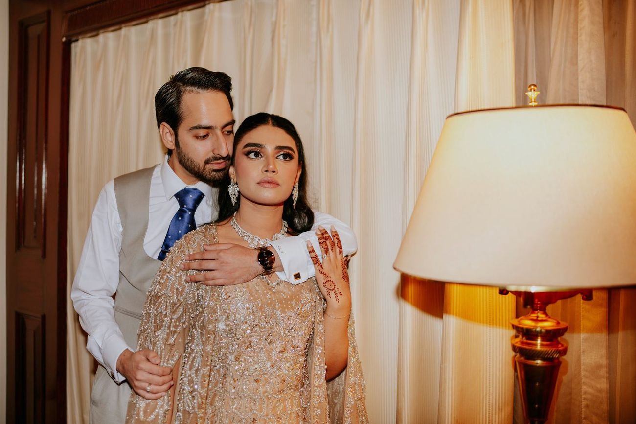 Groom standing behind the seated bride in the hotel suite, hand on her shoulder