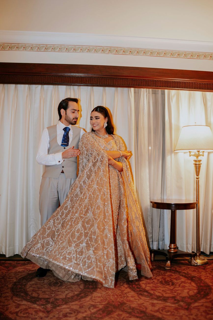 Bride mid-twirl in her beaded gown, groom watching her smile, hotel suite interior