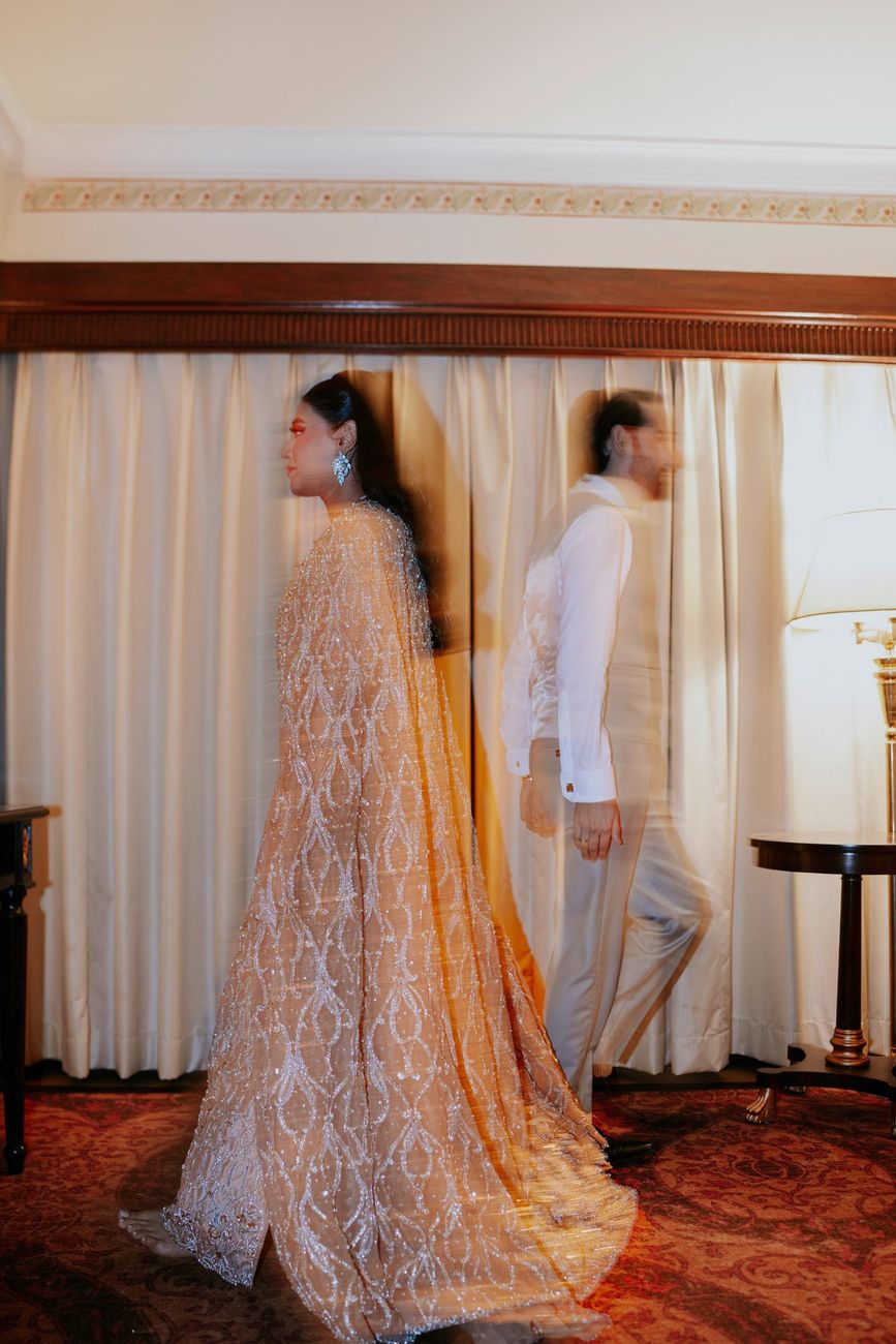 Artistic double-exposure shot of the bride and groom walking past each other in the hotel suite