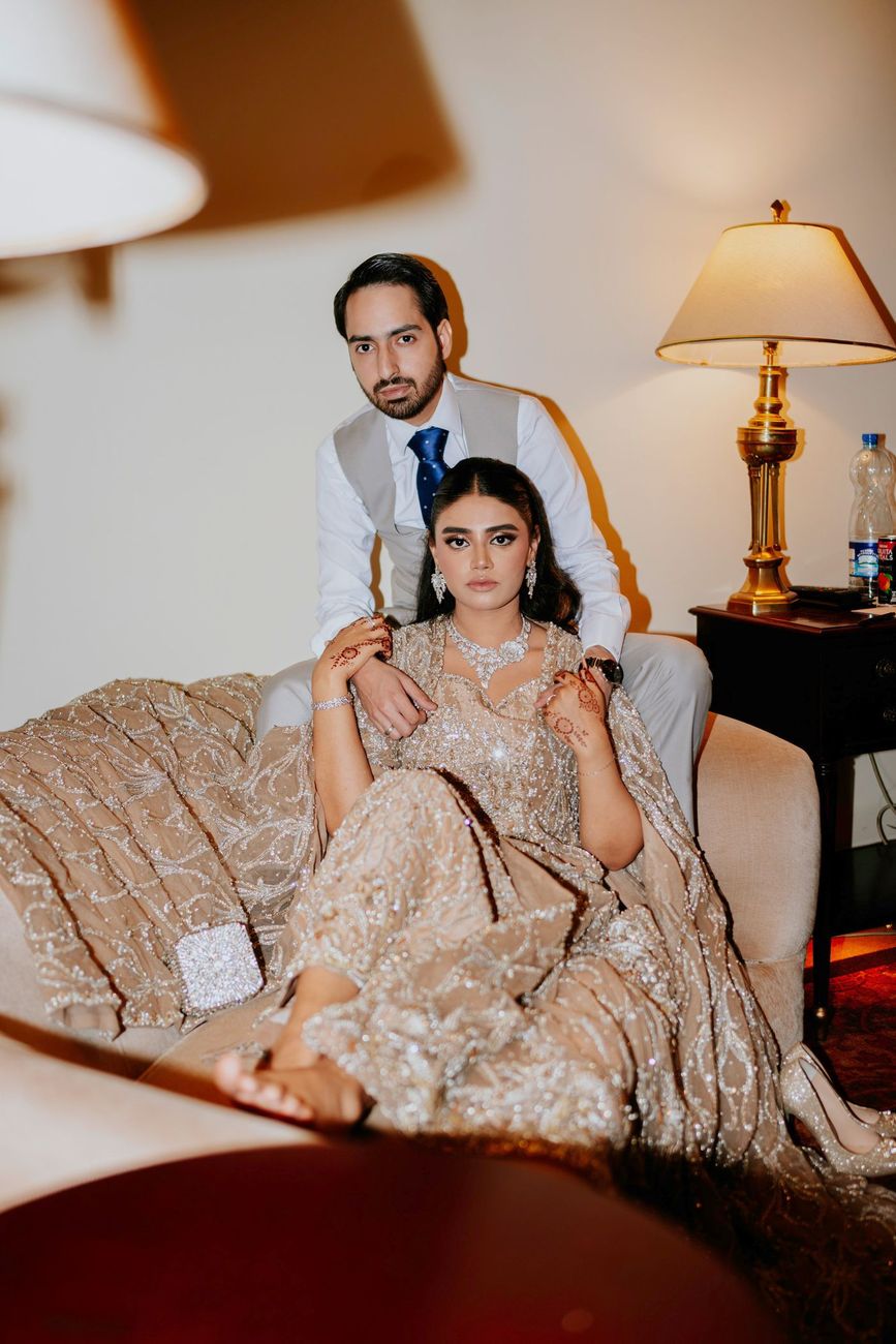 Bride reclining on the sofa as the groom stands behind her, hotel suite interior