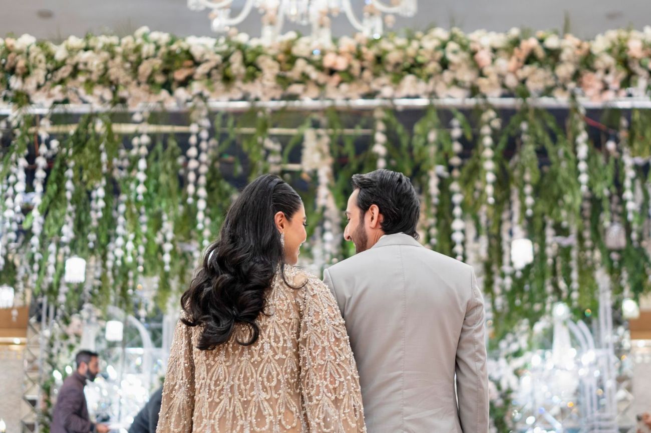 Close-up of the bride and groom from behind, smiling at each other in front of hanging greenery and floral strands