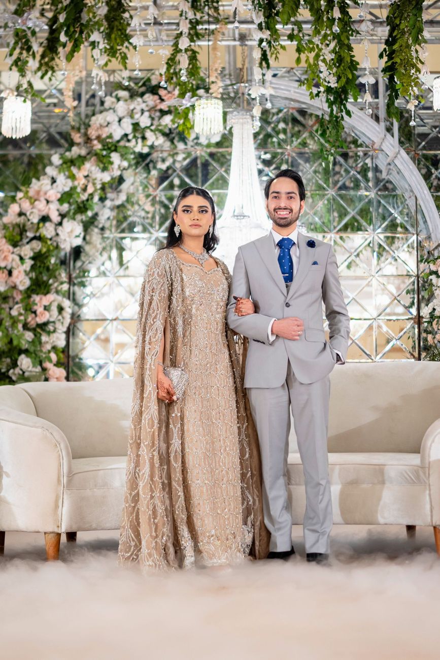 Bride and groom standing in front of a mirrored arched wall with hanging florals, fog rolling across the floor
