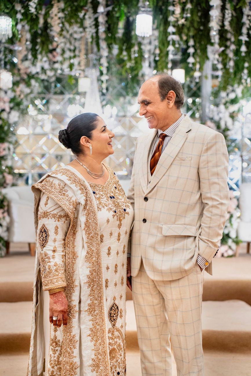Bride's parents smiling at each other in front of the reception's mirrored floral backdrop