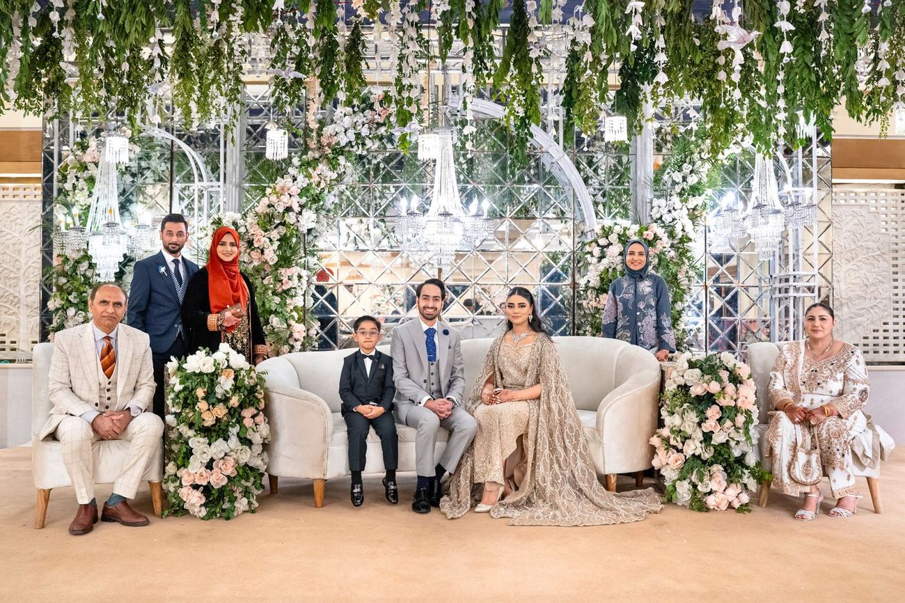 Family group portrait on a white sofa beneath a mirrored, greenery-draped backdrop at the reception