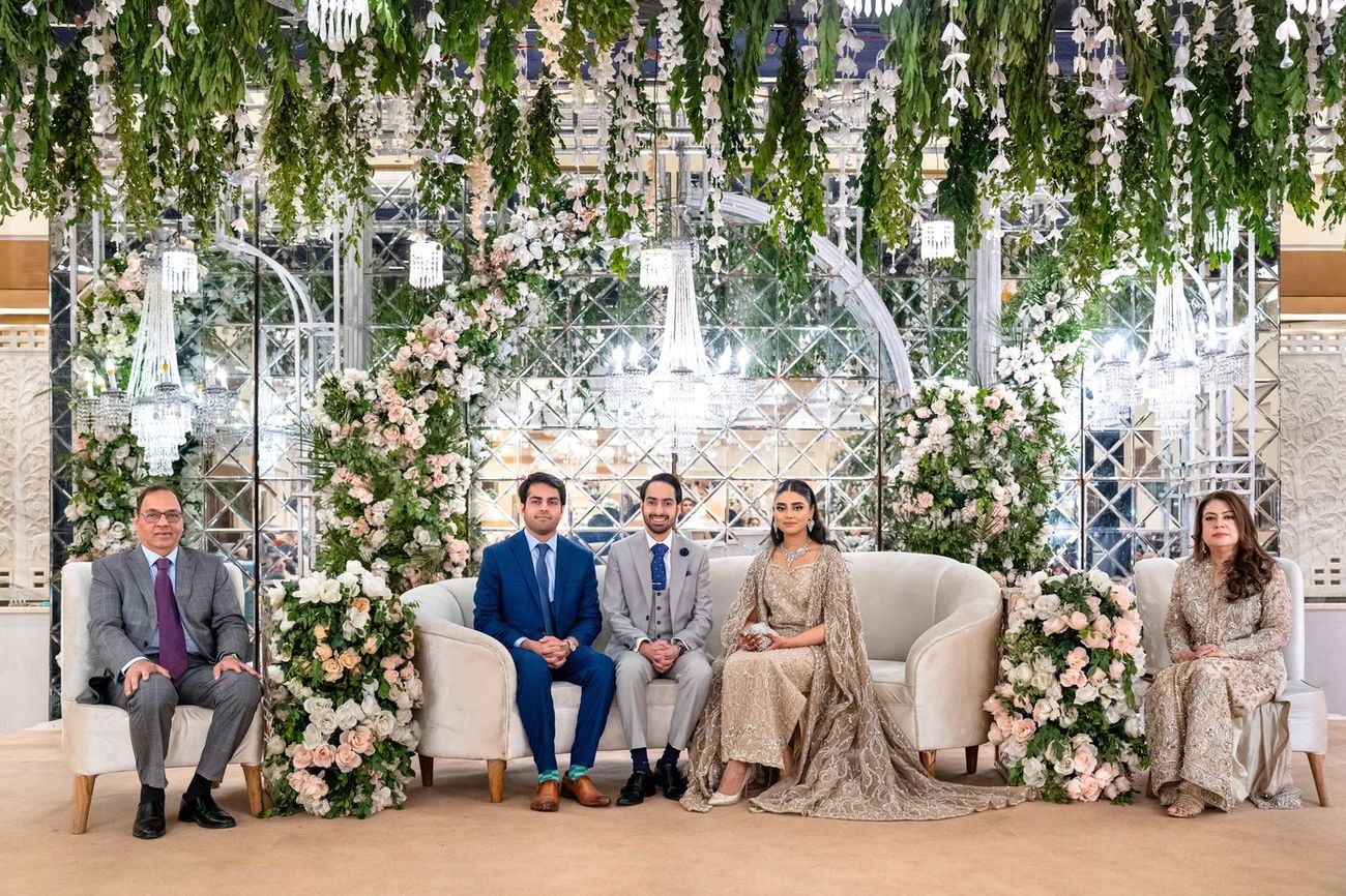 Extended family group portrait seated together beneath hanging florals and crystal chandeliers at the reception