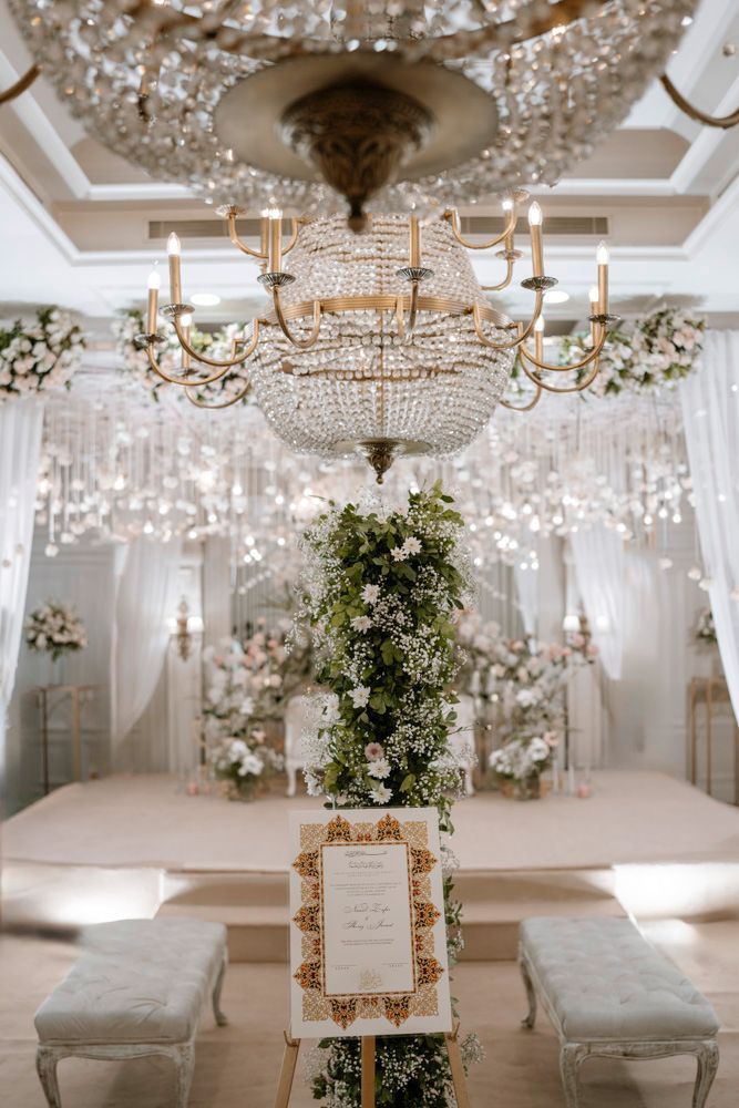 Wedding program signage displayed on an easel beneath a crystal chandelier and floral column, Sheraz & Nawal's wedding at Nishat Hotel, Lahore