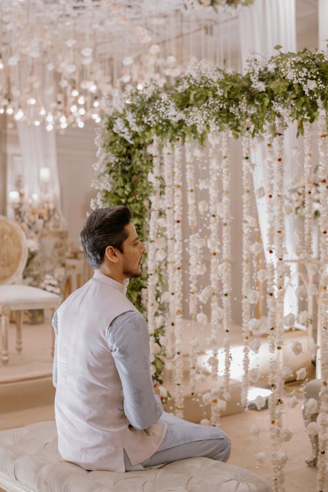 Groom seated in profile beside a floral and greenery archway, Sheraz & Nawal's wedding at Nishat Hotel, Lahore