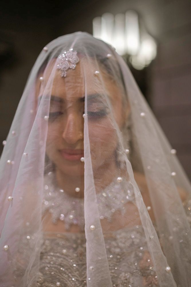Close-up of the bride beneath her veil, a floral hair ornament visible at her hairline, Sheraz & Nawal's wedding at Nishat Hotel, Lahore