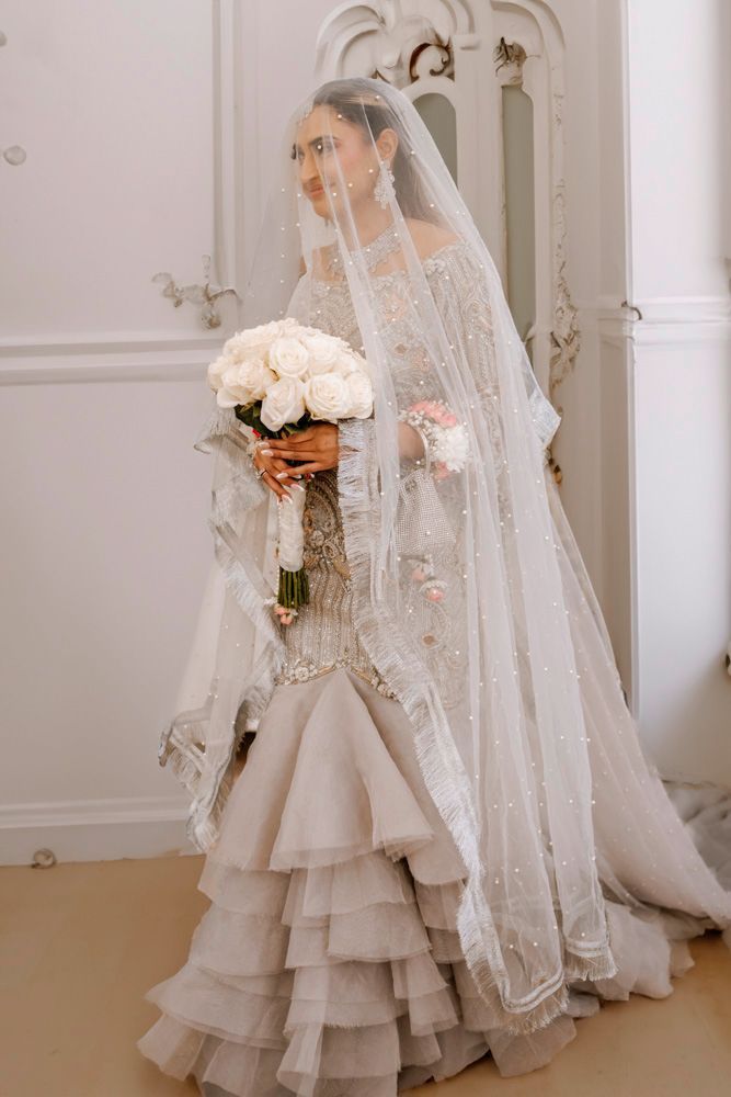 Solo bridal portrait in her ruffled mermaid gown, holding a white rose bouquet, Sheraz & Nawal's wedding at Nishat Hotel, Lahore