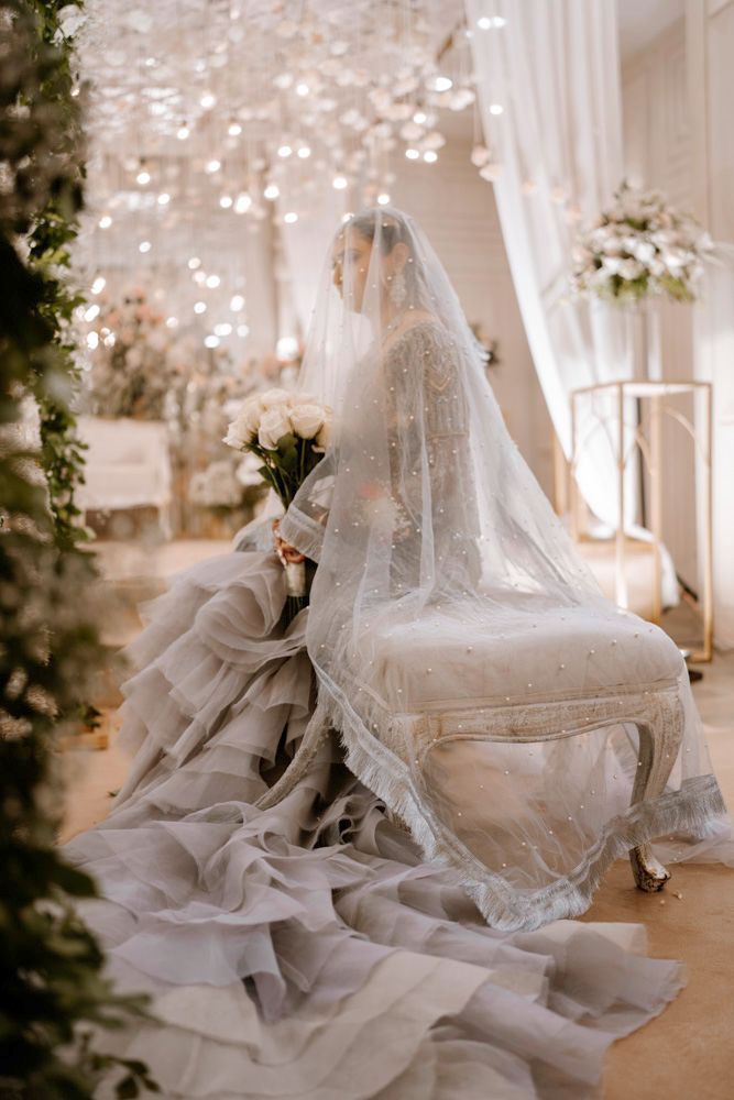 Bride seated on a chair beneath her veil, her ruffled gown train spread across the floor, Sheraz & Nawal's wedding at Nishat Hotel, Lahore