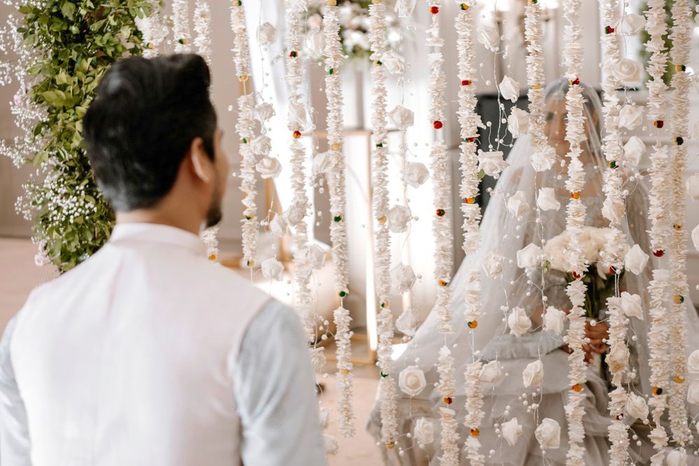 Groom viewed from behind watching the bride approach through a hanging floral curtain, Sheraz & Nawal's wedding at Nishat Hotel, Lahore