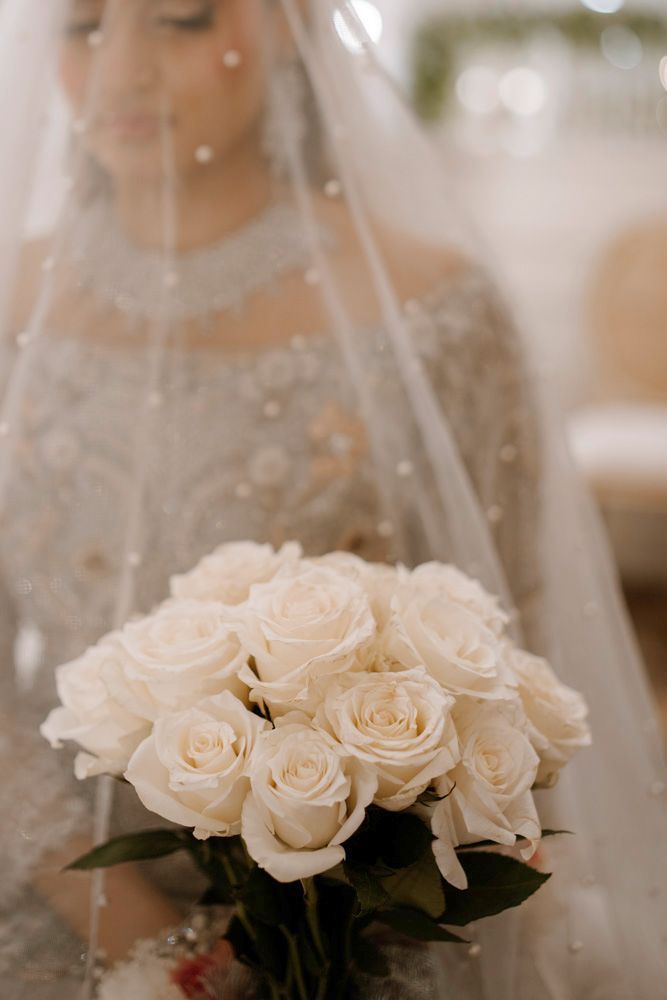 Close-up of a white rose bouquet held by the bride, her beaded gown softly blurred behind, Sheraz & Nawal's wedding at Nishat Hotel, Lahore