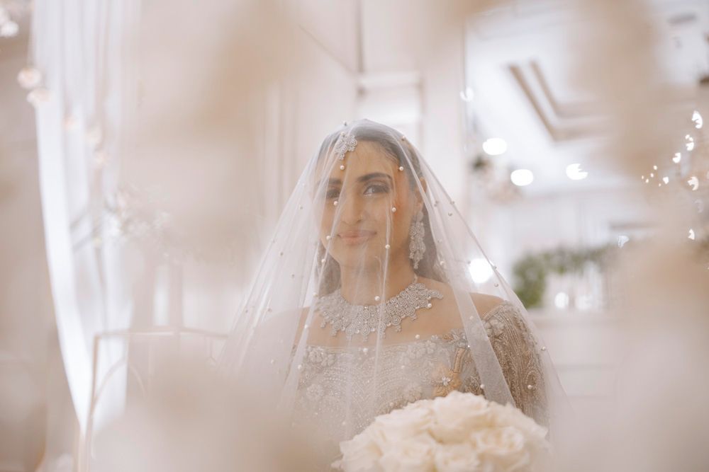 Close-up portrait of the bride smiling beneath her veil, framed by soft floral bokeh, Sheraz & Nawal's wedding at Nishat Hotel, Lahore