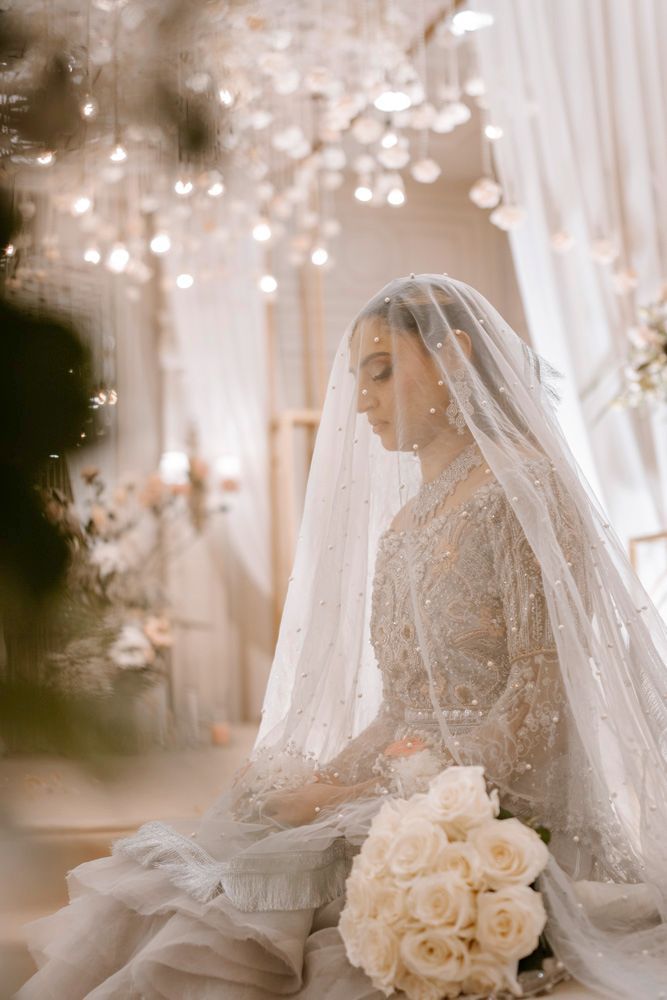 Bride seated in profile beneath her veil, holding a white rose bouquet, Sheraz & Nawal's wedding at Nishat Hotel, Lahore