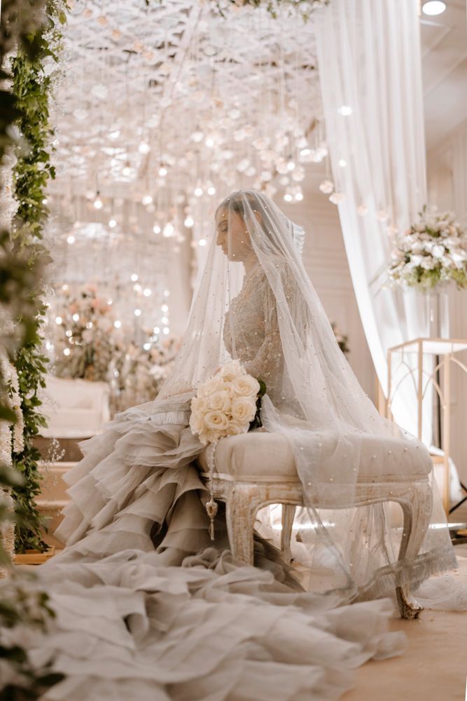 Bride seated on a tufted bench beneath her veil, ruffled gown train pooling on the floor, Sheraz & Nawal's wedding at Nishat Hotel, Lahore